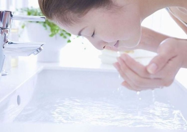 Người phụ nữ rửa mặt với nước ấm vào buổi sáng, chuẩn bị cho chu trình tẩy trang và rửa mặt đúng cách