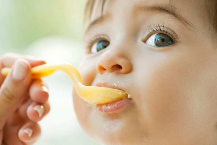 bàn tay mẹ đang đút váng sữa cho bé, cho thấy thời điểm và cách cho bé ăn váng sữa hiệu quả