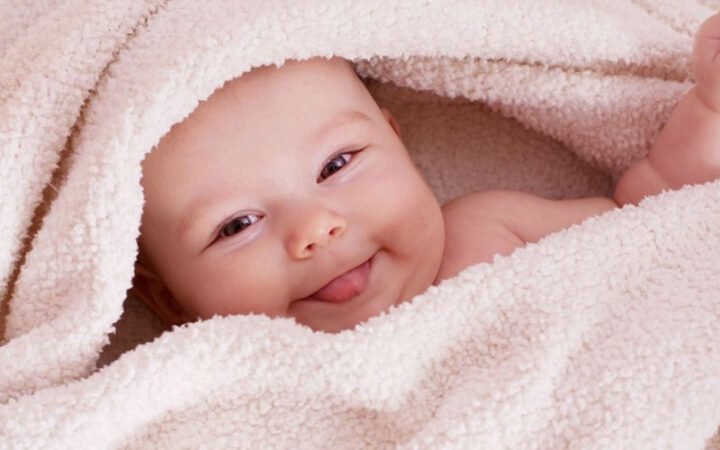 Bé 3 tháng tuổi đang nằm sấp trên thảm có họa tiết, tay chống cằm, mắt nhìn thẳng