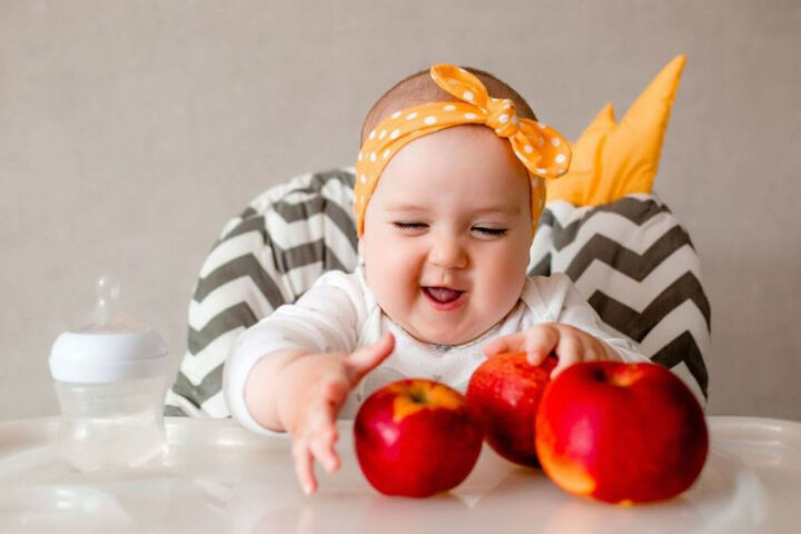 Bé gái 8 tháng cầm miếng táo tươi, loại trái cây giàu chất xơ tốt cho hệ tiêu hóa
