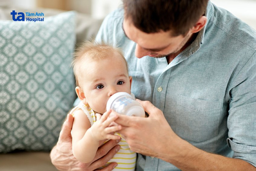 Bố hoặc người thân đang tập cách cho bé bú sữa bình, giúp bé làm quen