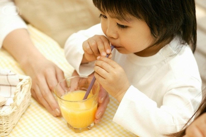 Em bé tươi cười cầm quả cam, biểu thị lợi ích của nước cam đối với hệ vi khuẩn đường ruột khỏe mạnh