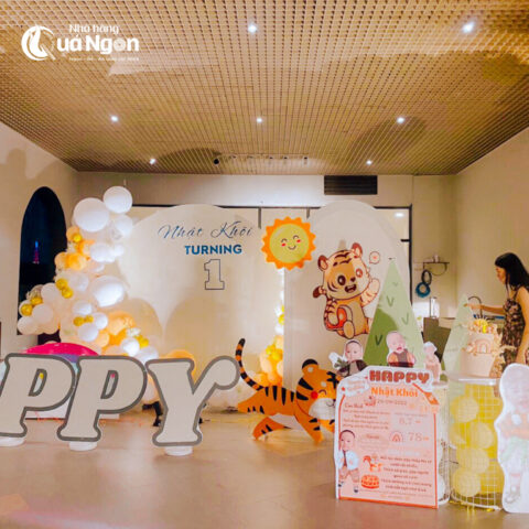 Góc trang trí tiệc thôi nôi tại nhà đơn giản nhưng đầy đủ, với khung ảnh kỷ niệm và bánh kem, thể hiện các bước chuẩn bị tỉ mỉ.