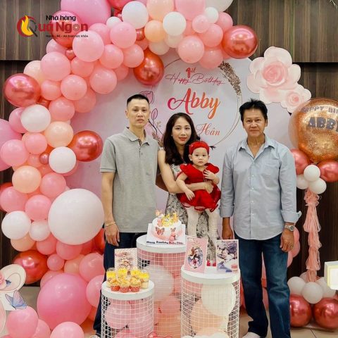 Hình ảnh tiệc thôi nôi ấm cúng tại nhà với bé trai thổi nến trên bánh kem, thể hiện ý nghĩa của bữa tiệc tròn một tuổi.