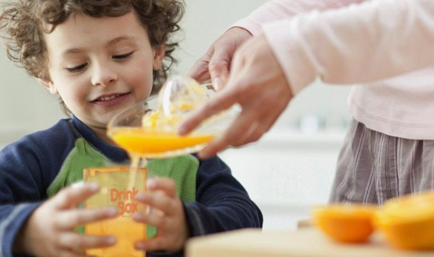 Một em bé đang uống nước cam, liên tưởng đến tác dụng ngăn ngừa bệnh ung thư ở trẻ