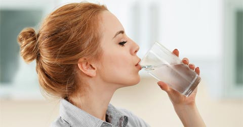Một phụ nữ đang uống nước lạnh, minh họa những điều không nên làm khi đến tháng để tránh đau bụng.