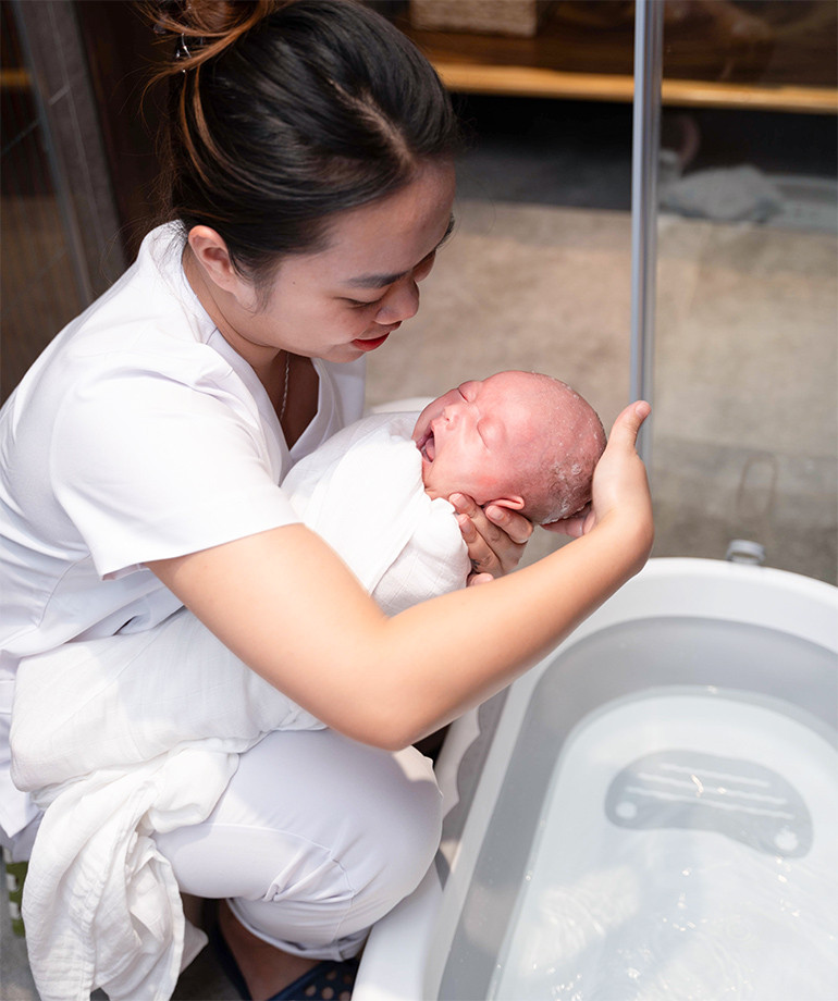 Người chăm sóc nhẹ nhàng gội đầu cho bé sơ sinh, bảo vệ mắt và tai trong quá trình cách tắm cho bé sơ sinh tại nhà.