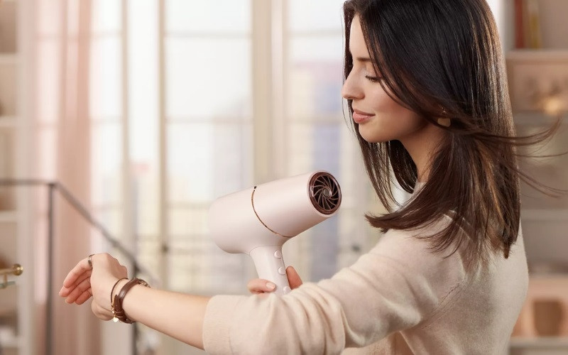 Người phụ nữ đang sấy khô tóc gọn gàng với máy sấy tóc mini tiện lợi