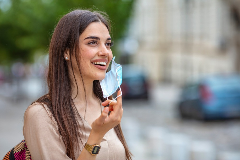 Người phụ nữ tháo khẩu trang y tế đúng cách bằng cách cầm dây đeo, hướng dẫn cách chọn và sử dụng khẩu trang
