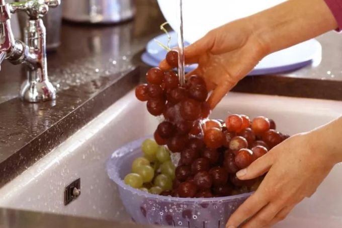 Phụ nữ mang thai rửa nho dưới vòi nước, minh họa cách vệ sinh nho sạch sẽ khi có bầu ăn nho được không và cần thận trọng.