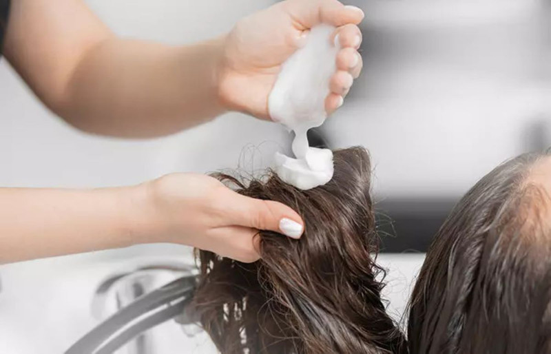 Tay đang thoa dầu xả lên mái tóc, bước chăm sóc quan trọng sau khi duỗi tóc để giữ ẩm và duy trì độ suôn mượt.