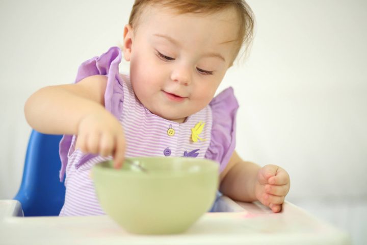 Trẻ nhỏ đang tập tự xúc ăn bằng muỗng trong bữa cơm gia đình